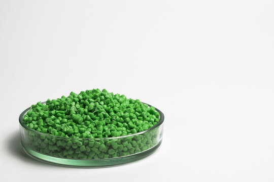 Green  granules of polypropylene or polyamide on a white background. Plastics and polymers industry. Copy space. Glass petri dish, flask, volumetric glassware, test tube.