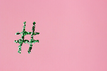 green shiny hashtag on a light pink background. Online technology concept and social media...