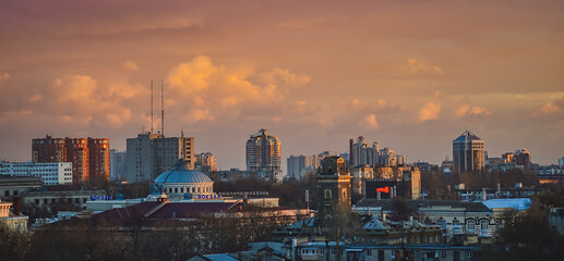 Fototapeta premium View from a height of the city at sunset. Evening Odessa overlooking the railway station. Dramatic sky over city streets. Aerial view panorama sunset city.