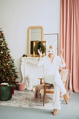 Obraz na płótnie Canvas Beautiful young woman in a carnival rabbit mask and white costume celebrates the new year near the Christmas tree in a modern interior. Inspiration. Soft selective focus.