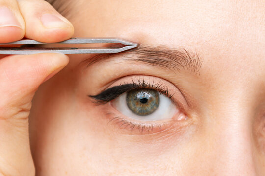 Close-up of the face of a young caucasian woman plucking eyebrows with tweezers. Eyebrow shape correction. Cosmetology, beauty