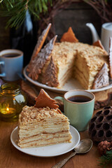 Napoleon cake decorated with Christmas gingerbread cookies. Fir branches, cones, candles, coffee, side view, wooden background.