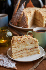 Napoleon cake decorated with Christmas gingerbread cookies. Fir branches, cones, candles, coffee, side view, wooden background.