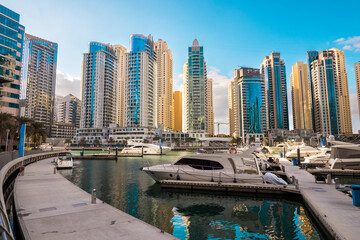 Beautiful view of the expensive yachts and motorboats moored at the piers of the Dubai Marina, surrounded by tall skyscrapers, Dubai, UAE
