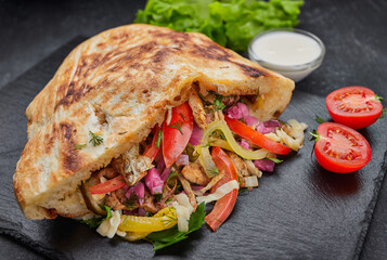 Giros, pita with chicken, sauce and vegetables, on a dark background