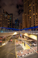 Fototapeta premium Night view of an oversized pedestrian bridge across a major road in the Dubai Marina district, Dubai, UAE, surrounded by skyscrapers