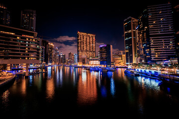 Obraz premium Scenic long exposure night view of the Dubai Marina with it's tall skyscrapers raising next to the yacht marinas and waterfront, Dubai, UAE