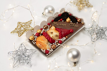 Christmas chocolate card with a figurine of a fox in a hat, on a white background with stars, balls and a garland, an inscription in Ukrainian, Happy Holidays