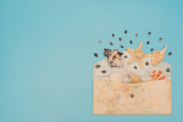 Different sea shells and starfish lay in opened envelope with map print on it on blue background. Flat lay style with copy space. Travel or summer concept
