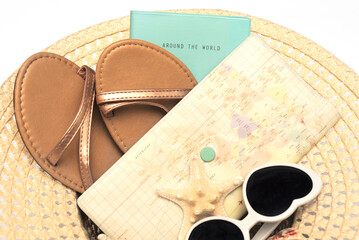 Travel items: flip flop sandals, sunglasses, notebook, envelope with shells lay in straw hat on white background. Flat lay style. Travel concept