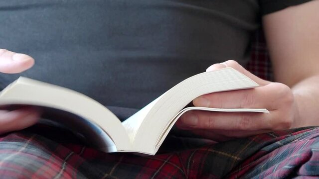 Man reading a book and turning page at home. Close-up of a person hands with an opened white book. Video 4k resolution