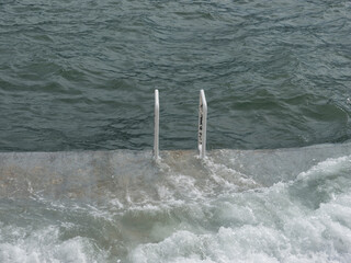 White handrails from cement beach to stormy sea water front view