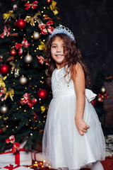 little curly girl at the Christmas tree with gifts new year lights garland