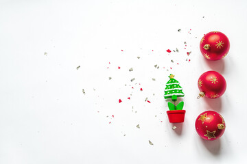 Top view of three red christmas balls, a fir tree model and confetti on a white background. Flat lay. Copy space.