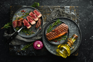 Grilled ribeye beef steak with rosemary, herbs and spices on a dark table. Free space for menus.