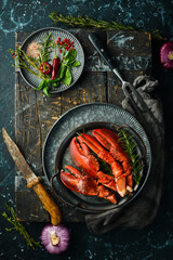 Boiled lobster claws with spices and herbs on a metal plate. On a black stone background.
