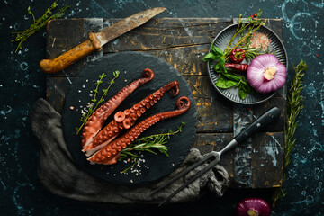 Boiled octopus tentacles with spices and herbs on a metal plate. On a black stone background.