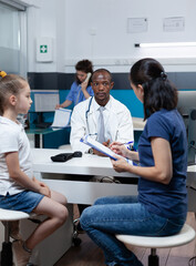 Patient mother writing medical accord on document while discussing sickness expertise with african...