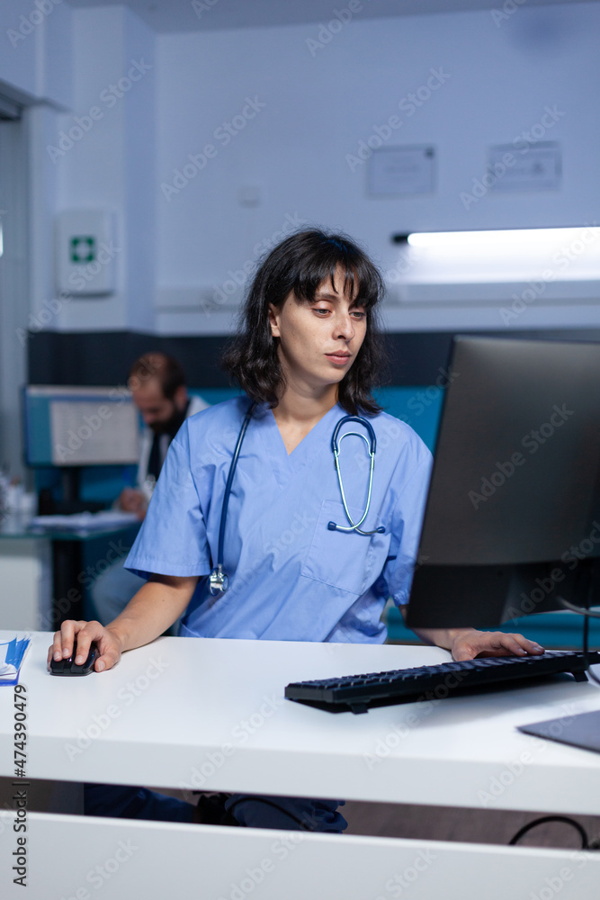 Poster medical assistant using computer at desk for work overtime. nurse in uniform looking at monitor for 