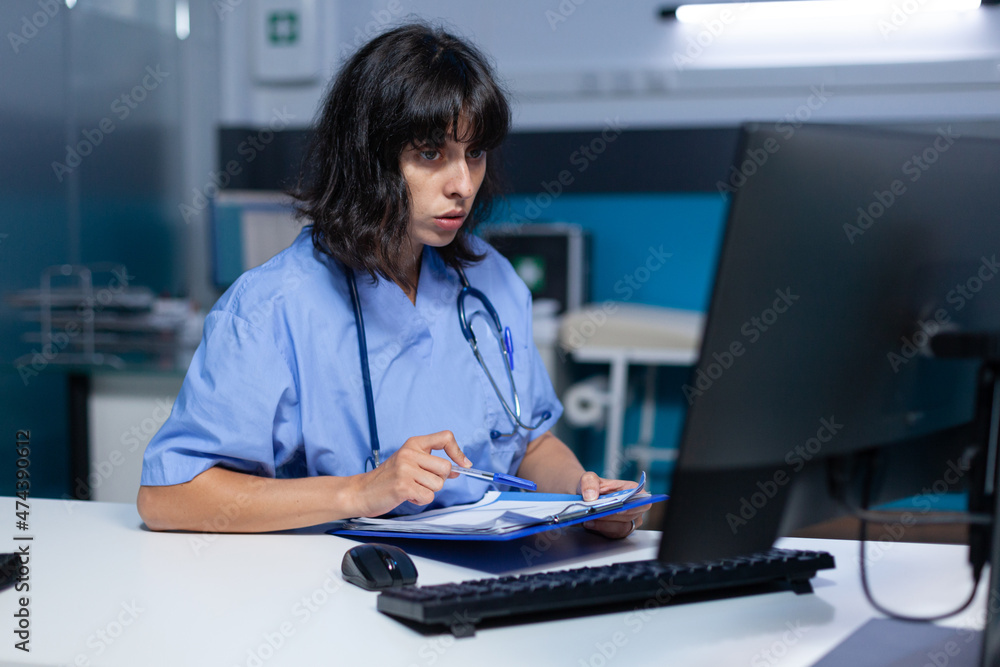 Poster medical assistant analyzing documents and files on monitor at night. nurse looking at computer and w