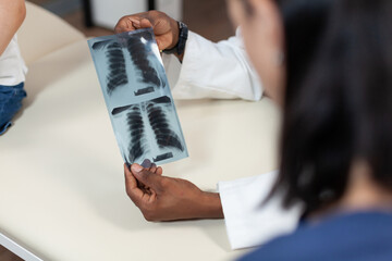 Closeup of african american pediatrician doctor holding lungs radiography in hand discussing medical results during consultation in hospital office. Therapist man analyzing xray. Medicine service