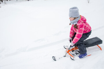 Fototapeta na wymiar Little girl on a sled having fun, with sled on the slope, fun and sun.