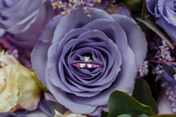Gold ring with gemstone among petals of Very Peri rose. Trendy color of the year 2022 in wedding. Engagement or proposal concept.