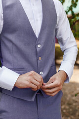 Man in Very Peri suit fastens the buttons of the jacket, close-up. Gentleman getting ready in the morning. Trendy color of the year 2022 in clothing.