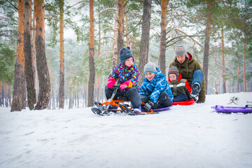 In winter, in the forest, children ride downhill on plastic plates.