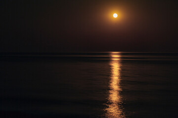 Obraz premium The Full Red Moon Shines Brightly in the Sky on a Dark Night Over the Calm Sea. Beautiful Moon Path on the Water