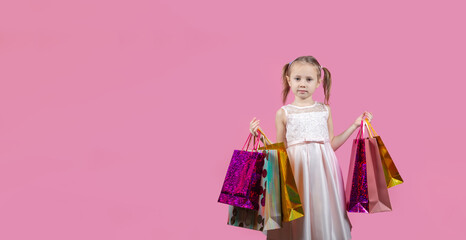 Cute little girl in a party dress on pink background holding colorful bags
