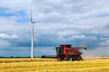 Farmer harvesting crops with clean energy producing wind turbines and storm clouds in background