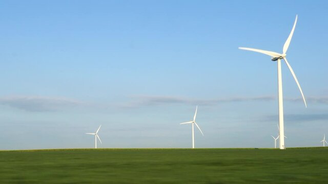 Wind turbine in a green field; tracking past turning white turbines with clear blue sky on early summer morning.  216B