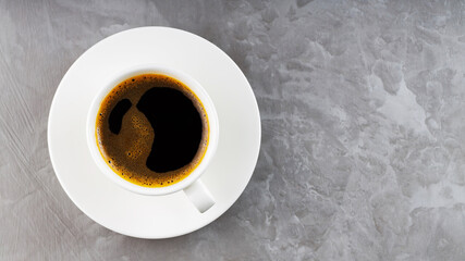 Cup of black coffee on a white saucer. Morning coffee in ceramic cup on a gray background. Top view. Copy space