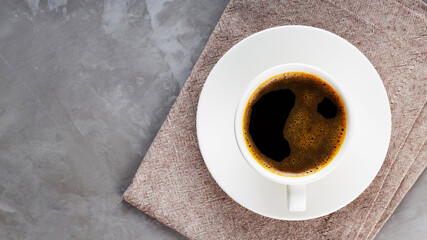 Cup of black coffee on a white saucer. Morning coffee in ceramic cup on a gray background. Top view. Copy space