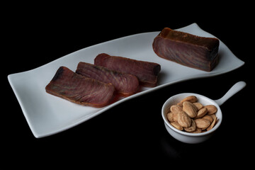 Several pieces of tuna jerky (mojama) on a plate accompanied by salted almonds.
