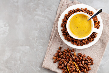 Cup of coffee with crema and coffee beans. Cup of coffee with a spoon and scattered coffee beans on a gray background. Roasted coffee beans in a white saucer. Copy space