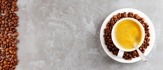 Cup of coffee with crema and coffee beans. Cup of coffee with a spoon and scattered coffee beans on a gray background. Roasted coffee beans in a white saucer. Copy space