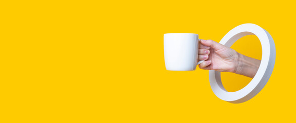 Female hand holding a white cup in a round hole on a yellow background. Banner.