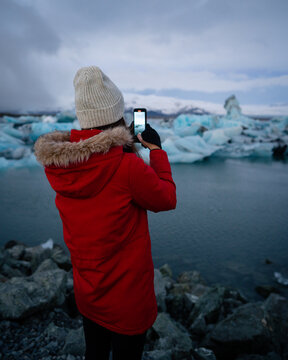 Girl taking a picture of a blue iceberg in ice lagoon at Iceland.  Woman taking photograph of beautiful Icelandic nature with Vatnajokull.
