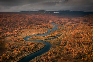 River with colourful trees in the countryside of Lapland at Stokenjokk Plateau in autumn in Sweden,...
