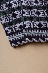 Knitted mittens on beige background. Warm handmade mittens for winter. Black pattern. Fringe close up