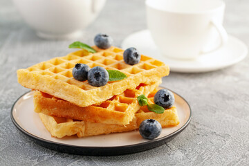 Homemade waffles with blueberries and mint on a bright background.