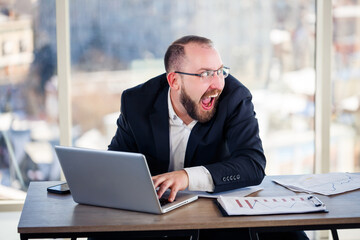 The corporate madman is sitting at the computer in the office and going crazy, the emotional portrait of the man at the table. Crazy worker at his workplace