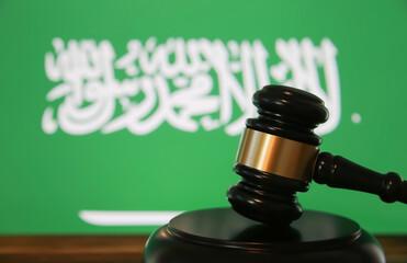 Closeup of isolated judge wood gavel with blurred saudi arabia flag background (focus on hammer head)