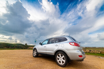 Fototapeta na wymiar Grey SUV under a dramatic sky in Sardinia