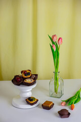 mini pasticcini serviti su appoggio alto bianco e fiori sullo sfondo