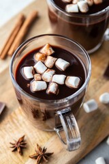 Two glass cups of hot chocolate with marshmallows and cinnamon sticks on wooden board and grey background. Winter food and drink concept. Selective focus.