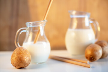 Vegan plant milk from potato in glass jar and potato tubers on the table. Concept of potato milk, vegan sustainable option, plant-based dairy. Substitute drink, healthy eating, diet, nutrition