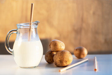 Vegan plant milk from potato in glass jar and potato tubers on the table. Concept of potato milk, vegan sustainable option, plant-based dairy. Substitute drink, healthy eating, diet, nutrition